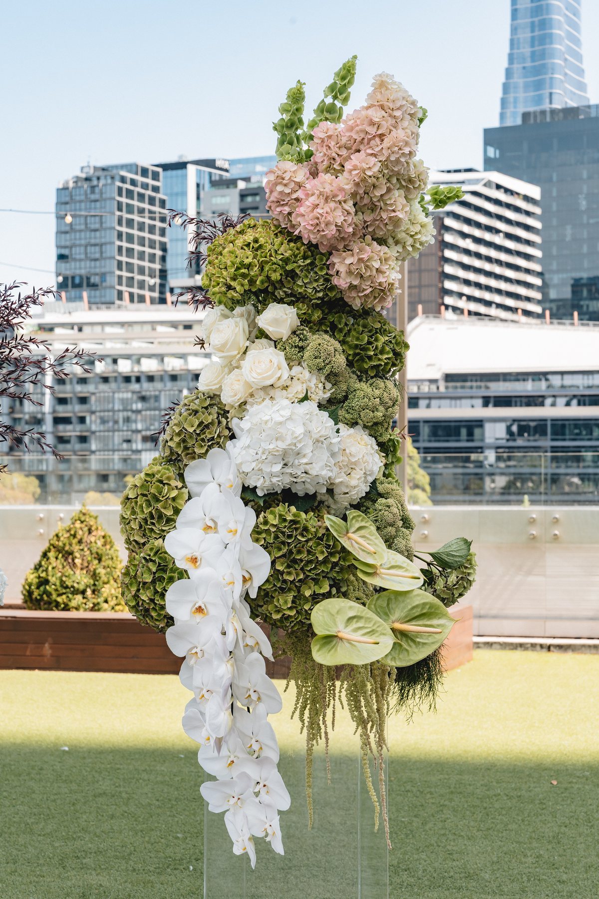 Crown Melbourne wedding — floral ceremony arch at Crown Aviary against the Melbourne skyline, by C2 Films
