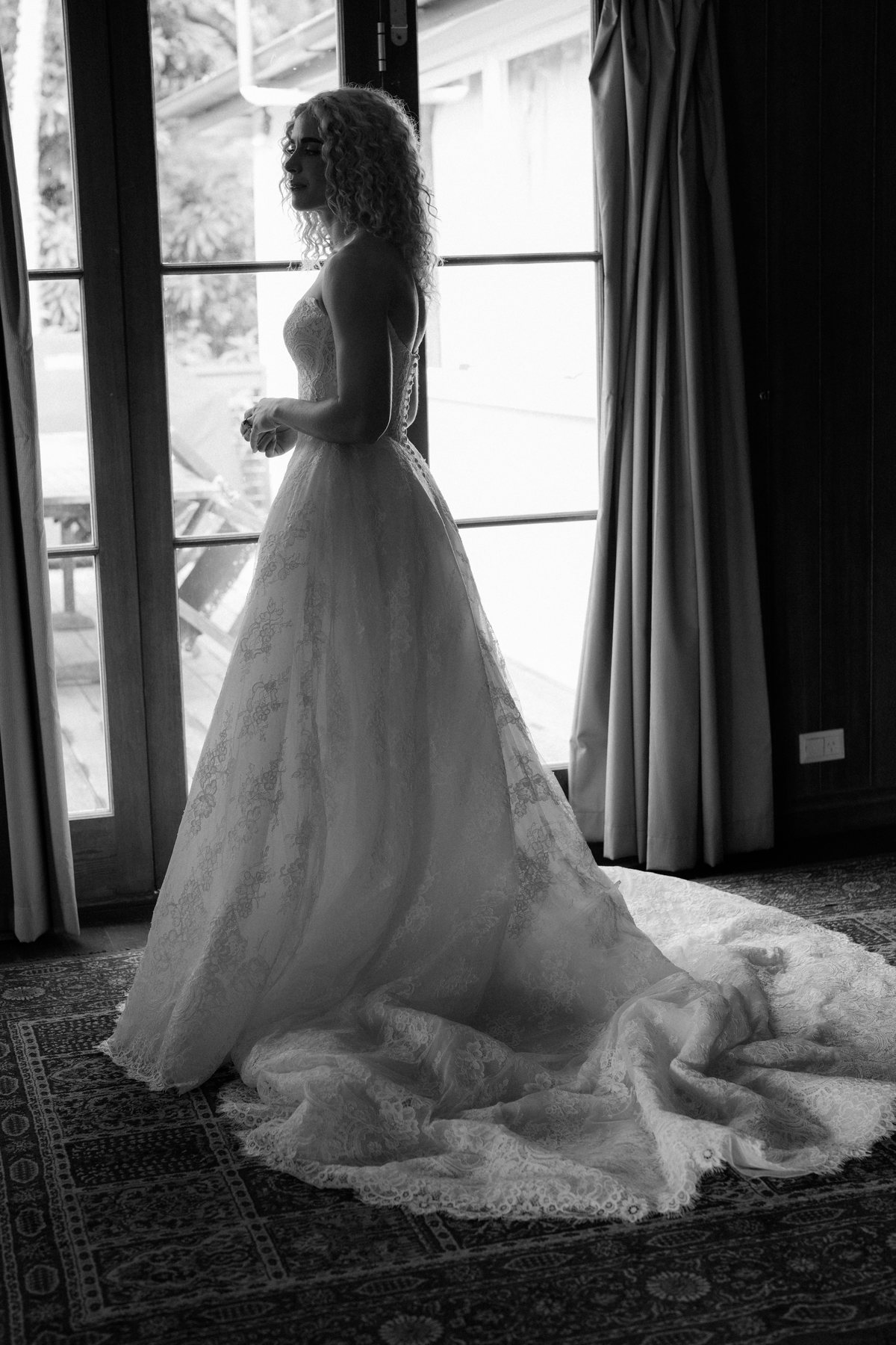 Monique at the window, the train of her gown across the rug at Rosewood Estate, Beechmont QLD — wedding photography by C2 Films