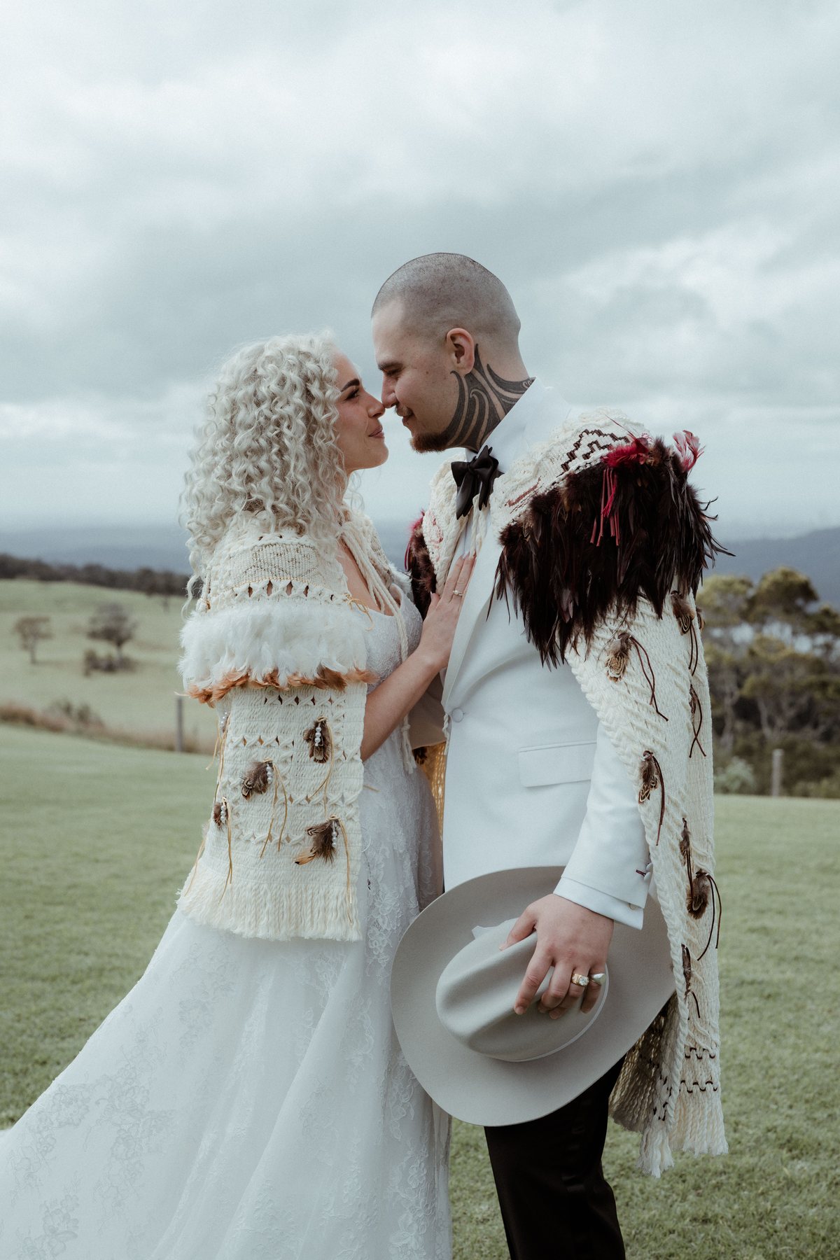 Kaleb and Monique nose to nose in korowai, hats in hand, at Rosewood Estate, Beechmont QLD — wedding photography by C2 Films
